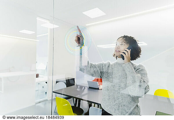 Businesswoman talking on smart phone and using projection glass screen at workplace