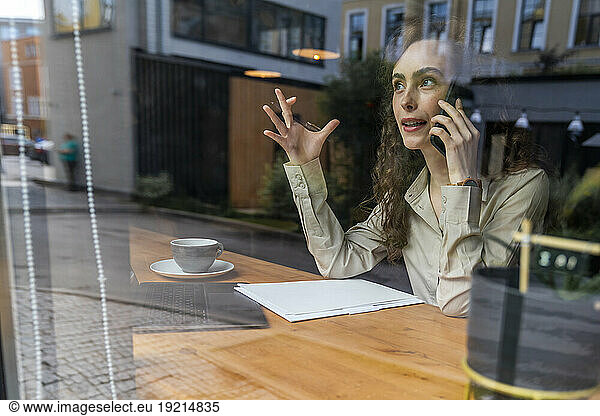 Businesswoman talking on smart phone at cafe seen through cafe