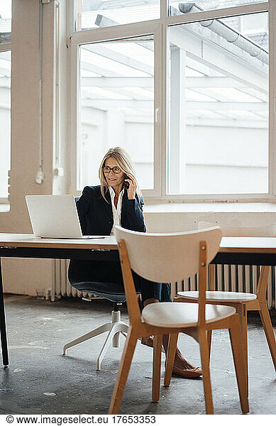 Businesswoman talking on smart phone at desk in office