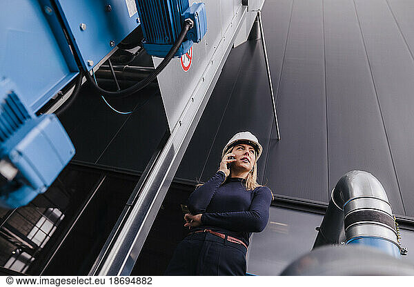 Businesswoman talking on smart phone near machine in factory