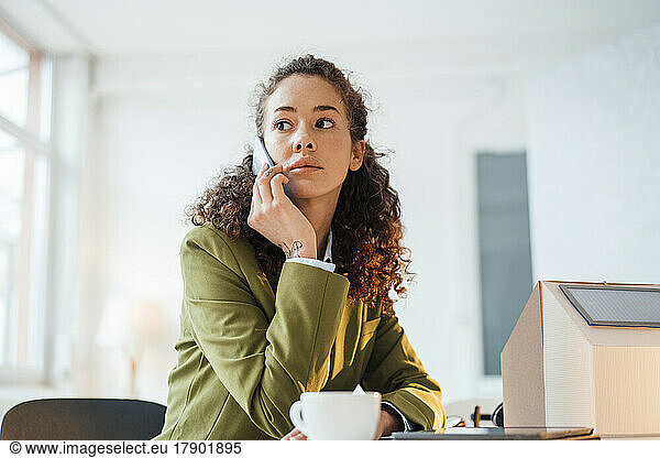 Businesswoman talking on smart phone sitting at desk in office