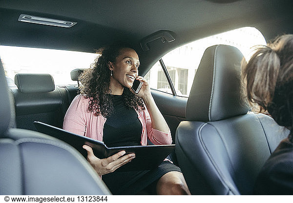 Businesswoman talking on smart phone while holding file in car