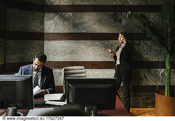 Businesswoman talking on smart phone while male colleague working at law office