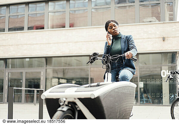 Businesswoman talking through smart phone sitting on cargo bike