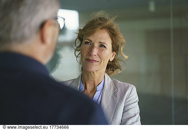 Businesswoman talking with businessman standing by glass wall