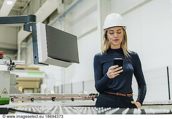 Businesswoman text messaging through mobile phone in factory