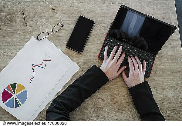 Businesswoman typing on laptop with eyeglasses and reports at desk in office
