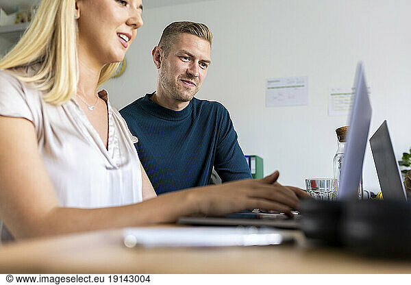 Businesswoman using laptop and discussing with colleague in office