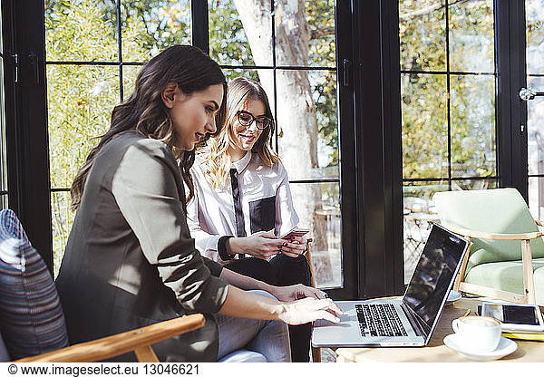 Businesswoman using laptop computer with colleague sitting in cafe