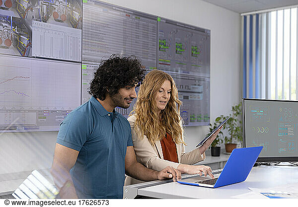 Businesswoman using laptop discussing with technician at desk in control room