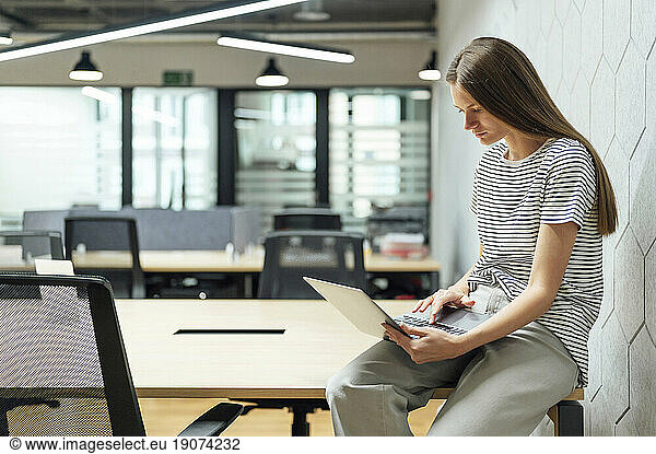 Businesswoman using laptop sitting on desk at office