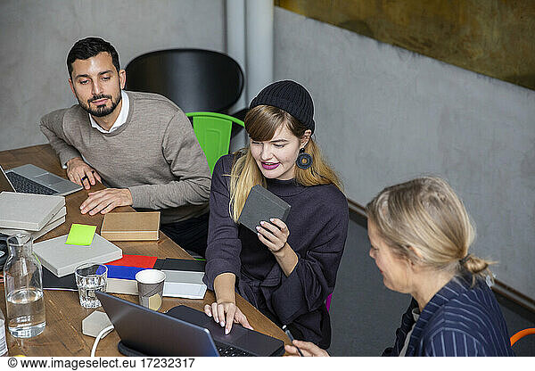 Businesswoman using laptop while discussing with male and female colleagues at creative office