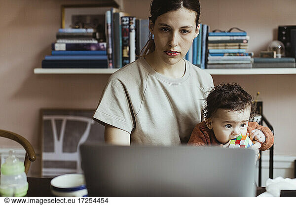 Businesswoman using laptop while sitting with baby boy at home