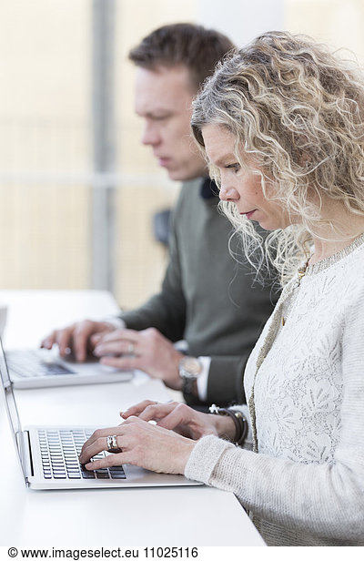 Businesswoman using laptop while sitting with male colleague in office
