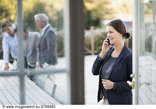 Businesswoman using mobile phone at patio with colleagues working in background