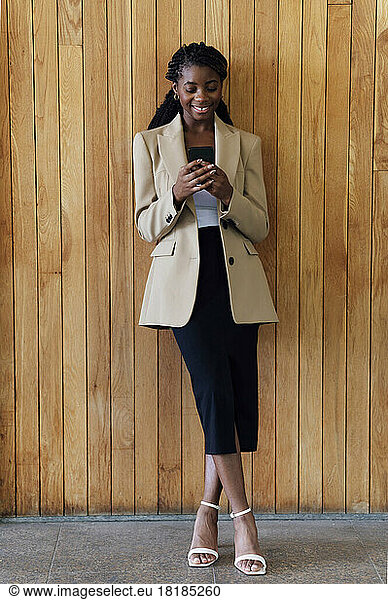 Businesswoman using mobile phone in front of wooden wall