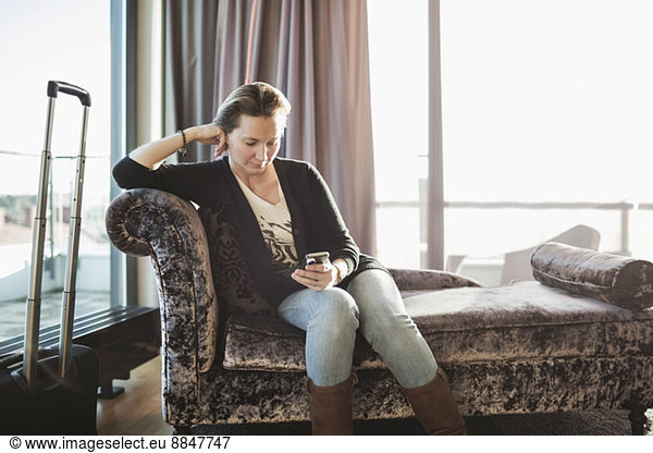 Businesswoman using mobile phone on chaise longue in hotel room