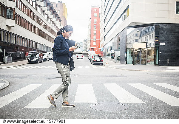 Businesswoman using mobile phone while crossing road