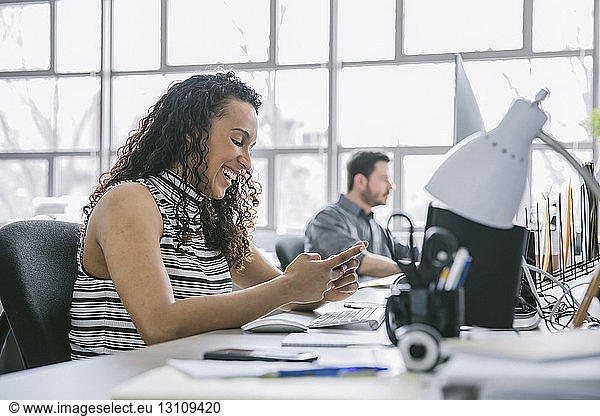 Businesswoman using mobile phone while male colleague working in background