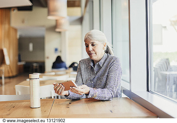 Businesswoman using mobile phone while sitting at office cafeteria