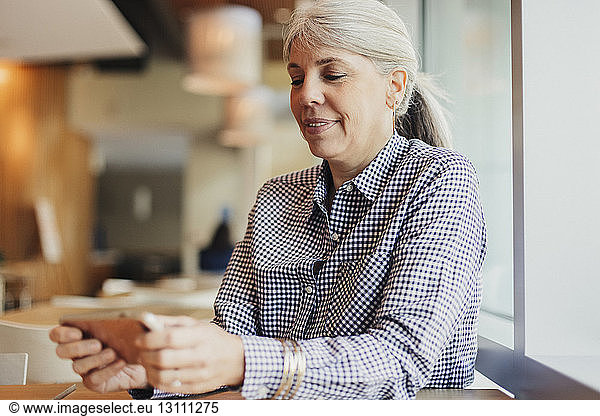 Businesswoman using mobile phone while sitting in cafeteria at office