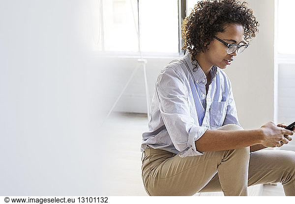 Businesswoman using mobile phone while sitting in lobby at office