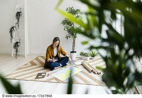 Businesswoman using mobile phone while sitting on carpet in office