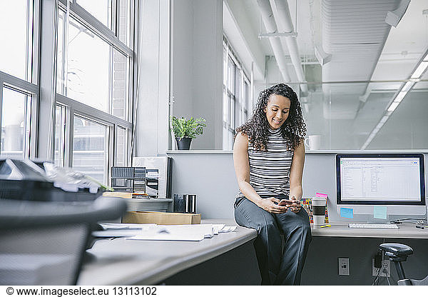 Businesswoman using mobile phone while sitting on desk in office
