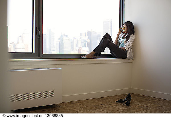 Businesswoman using mobile phone while sitting on window sill