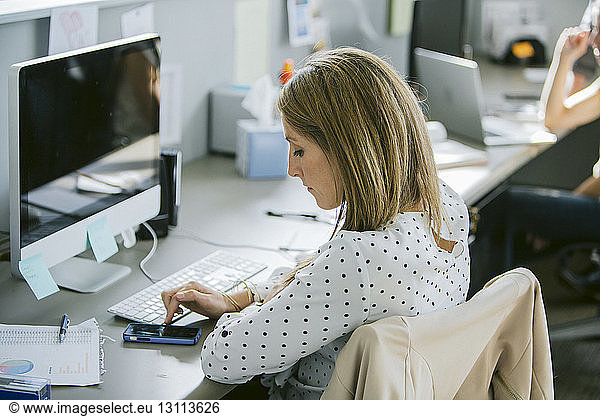 Businesswoman using mobile phone while sitting with colleague at desk