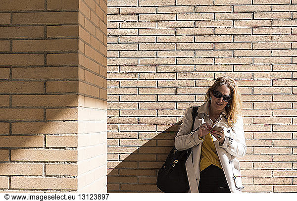 Businesswoman using mobile phone while standing by brick wall