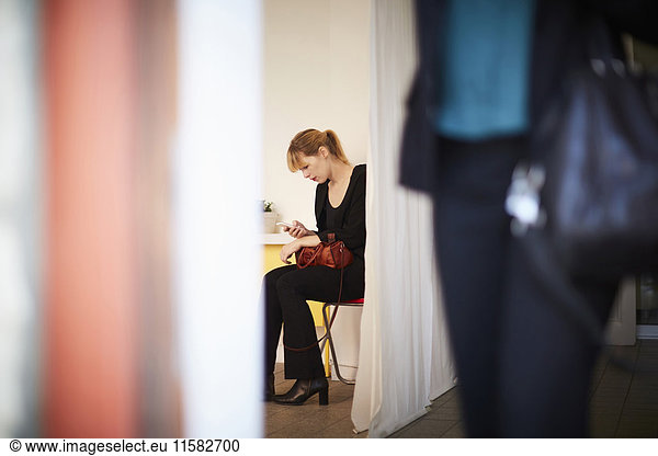 Businesswoman using mobile phone with colleague in foreground at office
