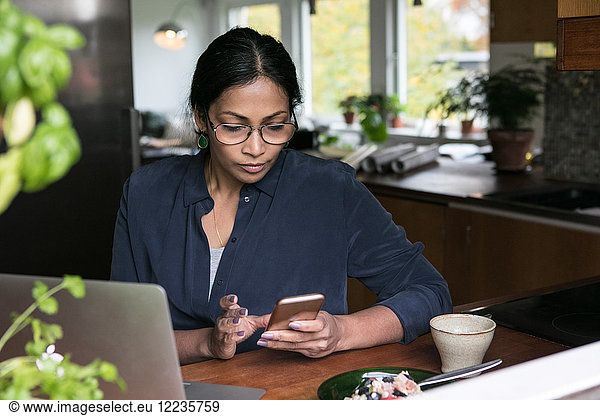 Businesswoman using mobile phone with laptop on table in home office