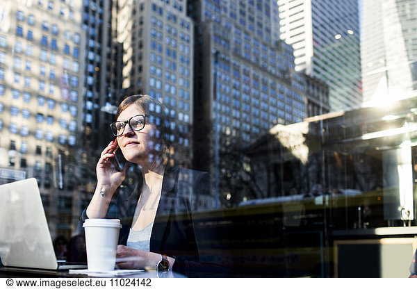Businesswoman using phone seen through window with reflection of building