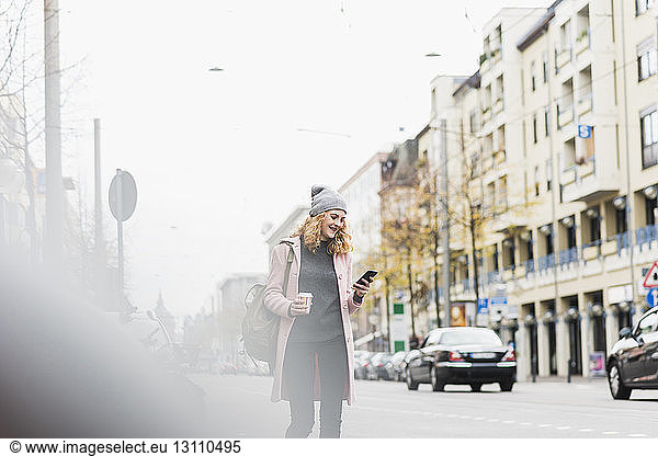 Businesswoman using phone while walking in city against sky