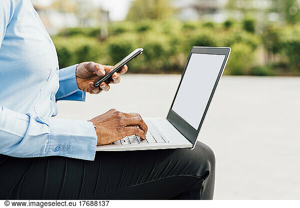 Businesswoman using smart phone sitting with laptop