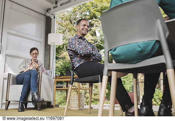 Businesswoman using smart phone while colleagues sitting on chairs in portable office truck