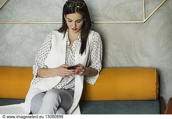Businesswoman using smart phone while sitting on sofa in hotel lobby