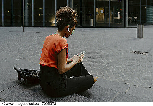 Businesswoman using smart phone while sitting on steps in city