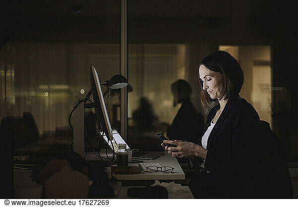 Businesswoman using smart phone while working overtime at work place