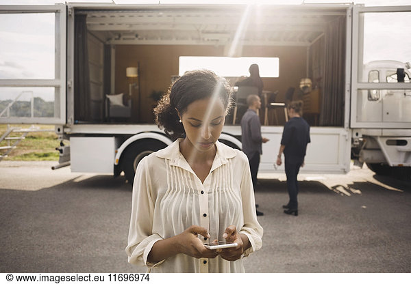 Businesswoman using smart phone with colleagues and portable office truck in background