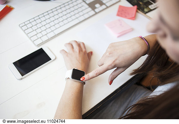 Businesswoman using smart watch while sitting at desk in office