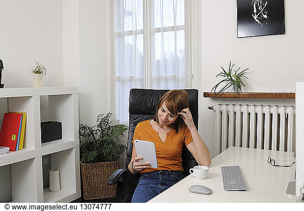 Businesswoman using tablet computer while sitting on chair at home office