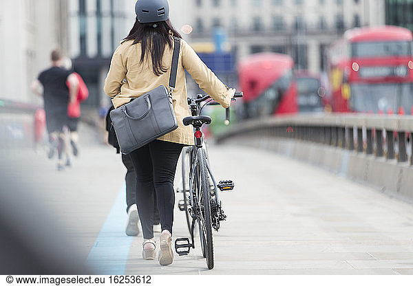 Businesswoman walking bicycle along city bridge  London  UK