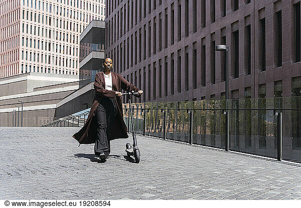 Businesswoman walking with electric push scooter in front of building