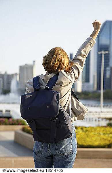 Businesswoman wearing backpack cheering with hand raised