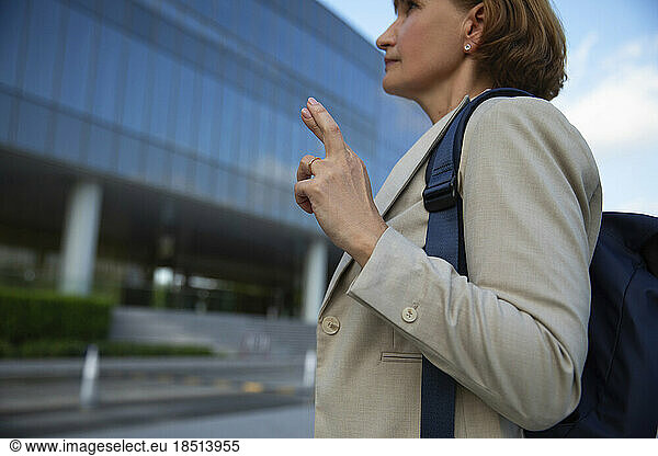 Businesswoman wearing backpack standing with crossed fingers
