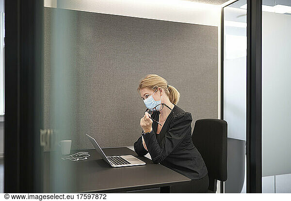 Businesswoman wearing face mask working on laptop at office desk