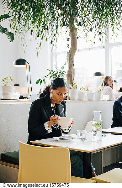 Businesswoman wearing headphones having soup at office cafe