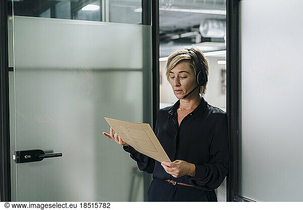 Businesswoman wearing headset reading document at office doorway